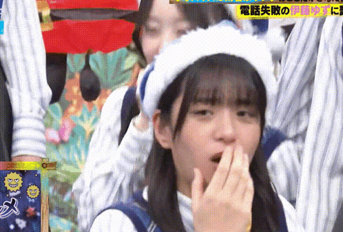 a girl wearing a hat is covering her mouth with her hand .
