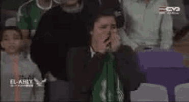 a group of people are sitting in a stadium watching a game and a man is covering his face with a green cloth .