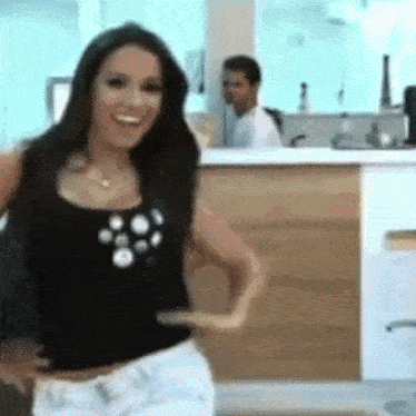 a woman in a black tank top and white shorts is dancing in front of a counter .