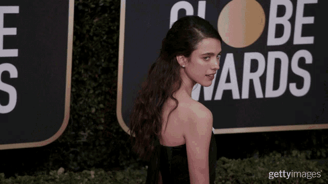 a woman in a black dress stands in front of a sign that says globe awards