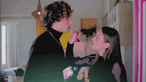 a woman applying makeup to a man 's face in a room