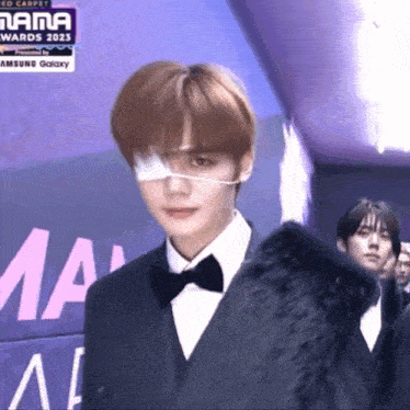 a man in a suit and bow tie is standing in front of a sign that says mama awards 2021
