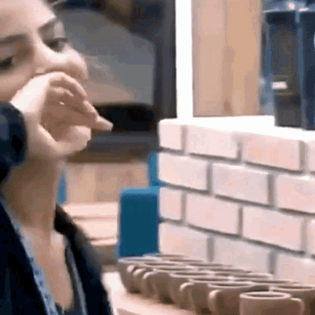 a woman is covering her mouth with her hand in front of a row of coffee cups