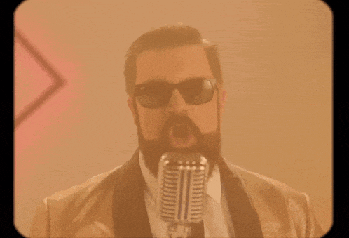 a man with a beard wearing sunglasses sings into a microphone