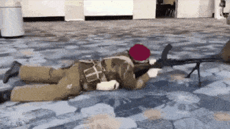a man is laying on the floor holding a rifle .