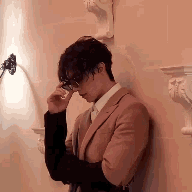 a man leaning against a wall adjusting his glasses