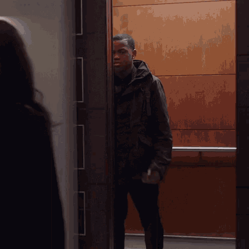 a man in a black jacket is standing in an elevator with a woman behind him