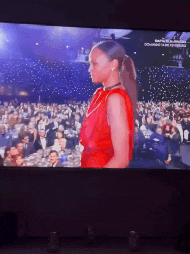 a woman in a red dress is standing in front of a crowd on a tv screen
