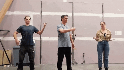two men and a woman are standing in front of a wall and pointing at something