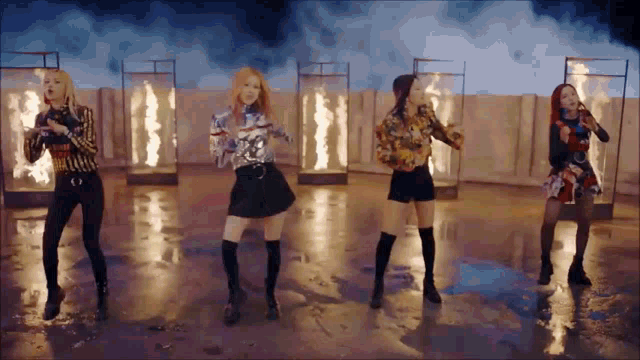 a group of women are dancing in a room with flames behind them .