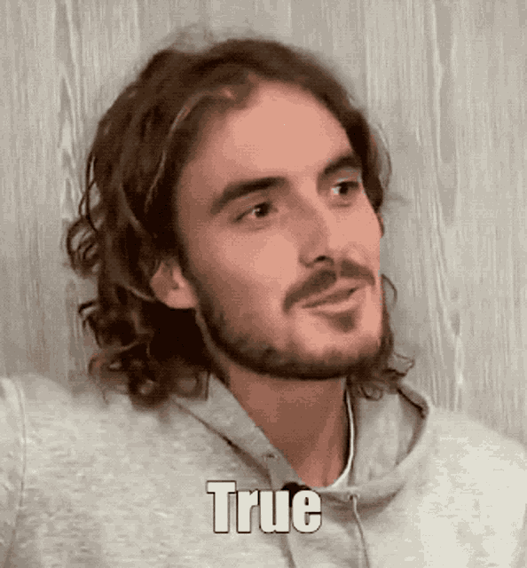 a man with long hair and a beard is wearing a grey hoodie that says true on it