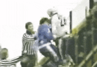 a group of people are standing around a man in a blue shirt with the number 12 on it .
