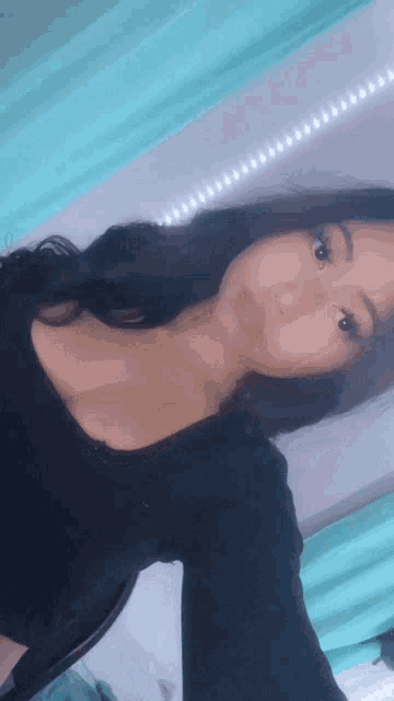 a woman in a black top is taking a selfie in front of a blue curtain .
