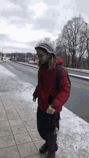 a person wearing a red jacket and a hat is walking down a snowy sidewalk
