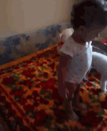 a little girl is standing on a bed with a floral blanket