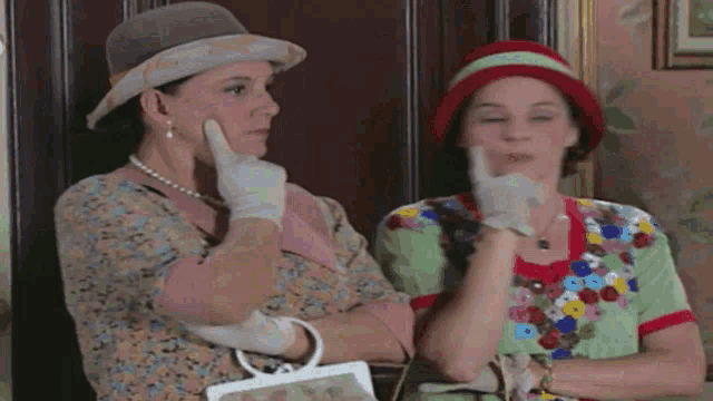 two women wearing hats and gloves are sitting together