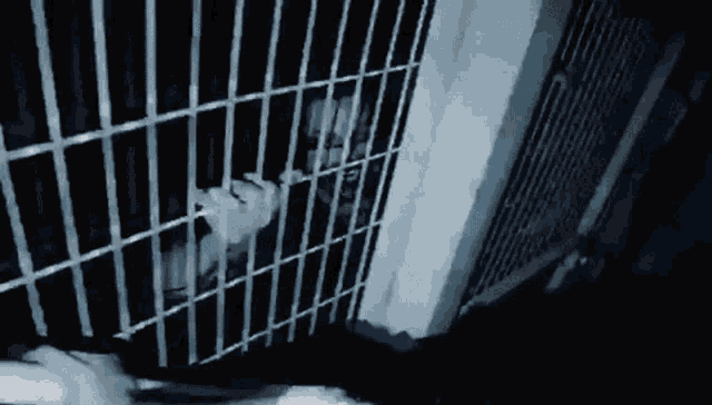 a man is behind bars in a jail cell with his hands behind bars .