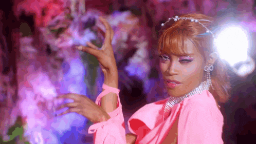 a woman in a pink dress is dancing with her hands in the air