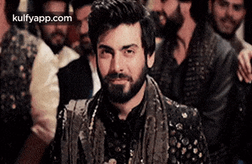 a man with a beard is sitting in a crowd of people and smiling .