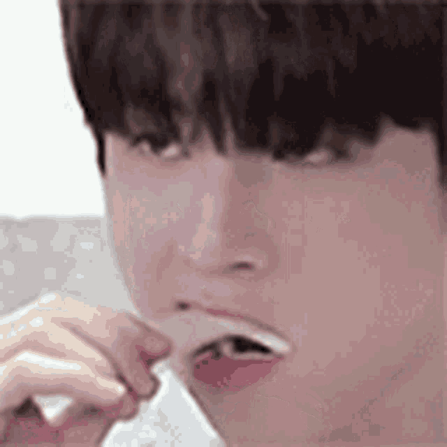 a young man is brushing his teeth with a toothbrush while holding a piece of paper in his mouth .