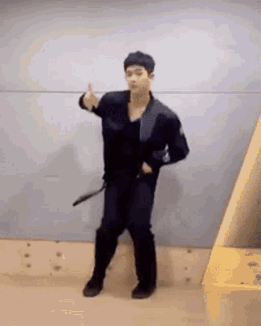 a man in a black jacket and black pants is dancing in front of a wall