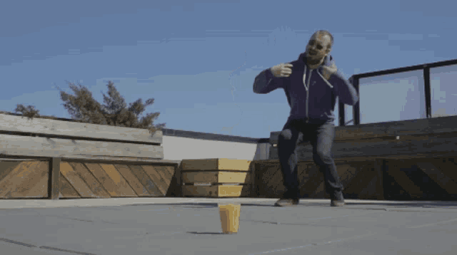 a man in a purple sweatshirt throws a yellow cup in the air