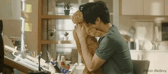 a man is sitting at a desk holding a cat in his lap .