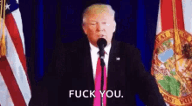 a man in a suit and tie is standing in front of a microphone and saying fuck you .