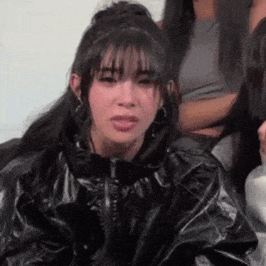 a woman in a black jacket is making a funny face while sitting in front of a group of women .