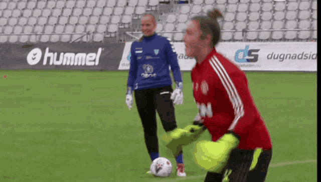 two female soccer players on a field with a hummel ad in the background