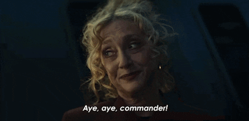 a woman with curly hair says aye aye commander in a dark room