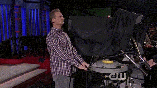 a man in a plaid shirt is standing in front of a camera that says ew