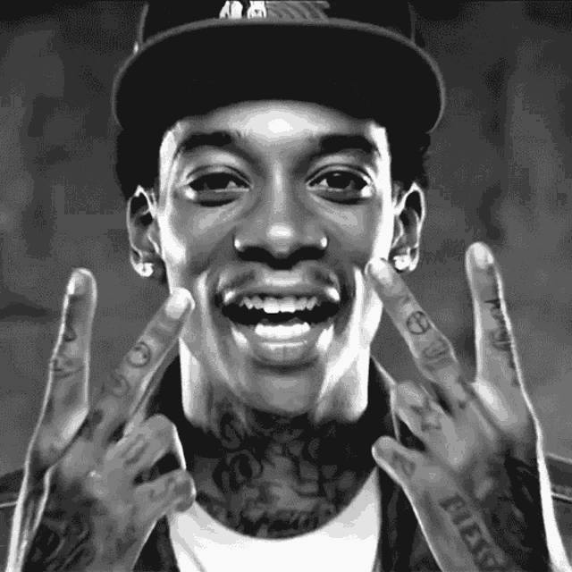a black and white photo of a man wearing a hat and making a peace sign