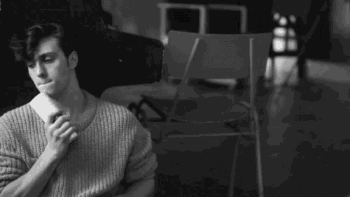 a black and white photo of a man in a sweater sitting on the floor