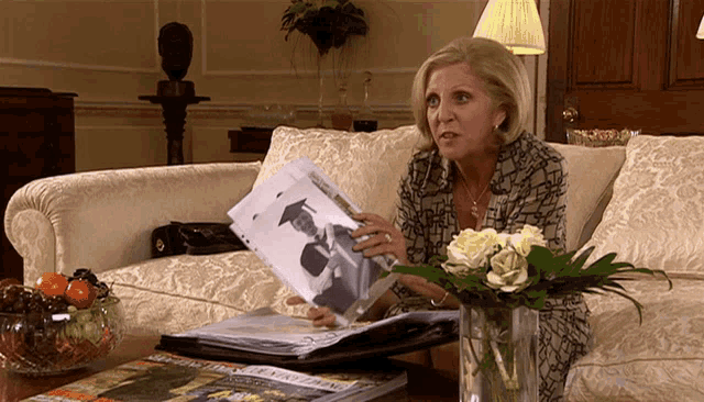 a woman sitting on a couch holding a picture of a man in a graduation cap