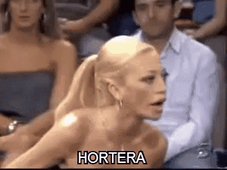 a woman in a strapless dress is sitting in a crowd with the word hortera written on her chest .