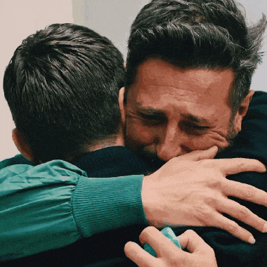 a man with a beard is hugging another man with his eyes closed
