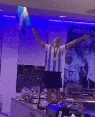 a man in a argentina jersey is standing in front of a blue wall with his arms in the air .