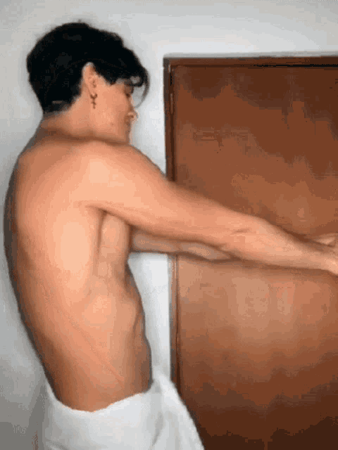 a shirtless man wrapped in a white towel is standing in front of a wooden door .