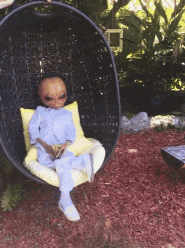 an alien is sitting in a wicker chair outside