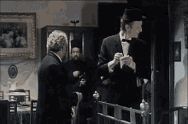 a man in a tuxedo and bow tie is talking to another man