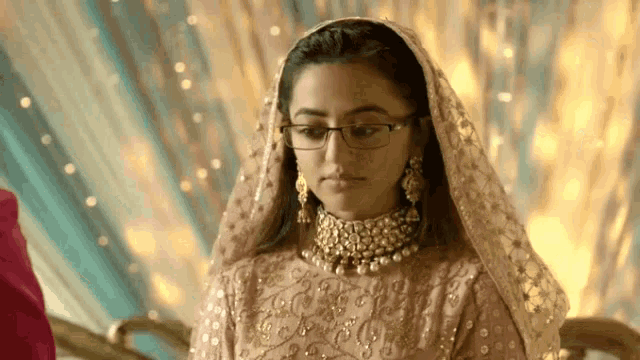 a woman in a wedding dress and veil is wearing glasses and a necklace .
