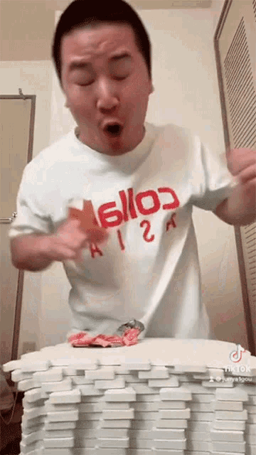 a man wearing a t-shirt that says hello on it is standing next to a pile of dominoes