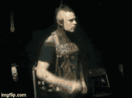 a man in a black shirt is standing in a dark room with his fist up .