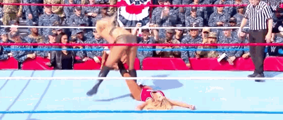 a woman is laying on the ground in a wrestling ring while a referee looks on .
