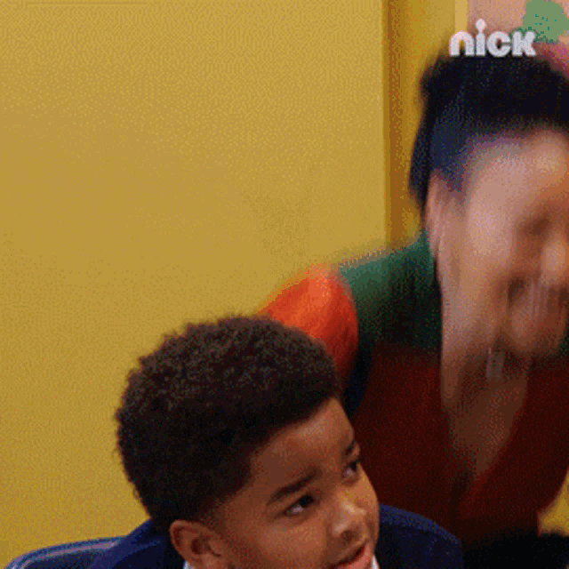 a boy and a woman are sitting in front of a yellow wall with nick written on the bottom