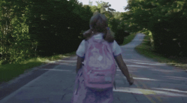 a girl with a backpack is walking down the road