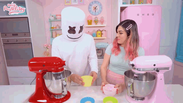 a pink smeg refrigerator sits in a kitchen next to two mixers