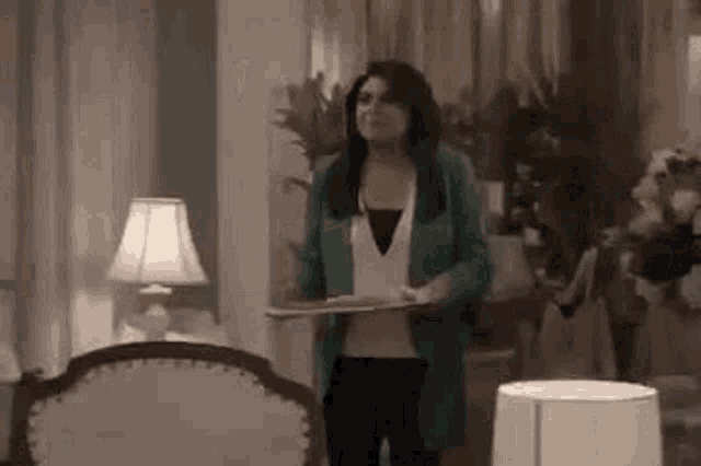 a woman in a green jacket is standing in a living room holding a tray .