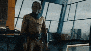 a man in a yellow and blue superhero costume is standing in front of a large window .